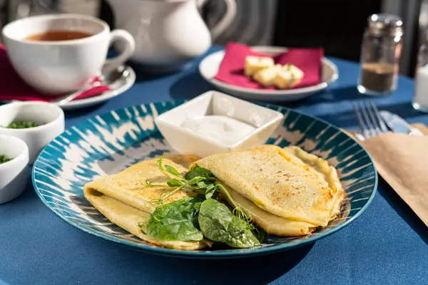 Ispanaklı krep ve güzel mavi beyaz bir tabakta servis edilen Yunan yoğurdu. Sabah güneşiyle aydınlatılan bir kahvaltı seti.