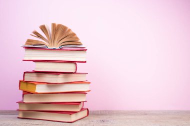 Sert kapaklı kitaplar, tahta güverte masasında sayfalar ve pembe arka planlı kompozisyon. Kitaplar istifleniyor. Okula dönelim. Uzayı kopyala Eğitim geçmişi. Okul taksiti.