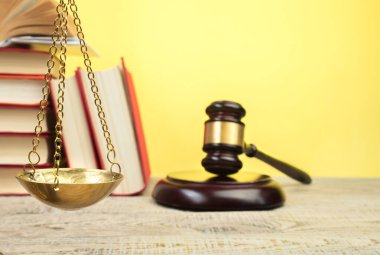 Hukuk konsepti - açık hukuk kitabı, yargıç tokmağı, teraziler, mahkeme salonundaki ya da kolluk kuvvetlerindeki heykel. Tahta masa, sarı arka plan..