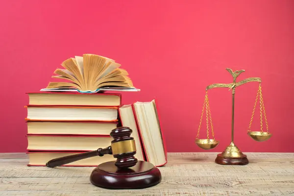 Law concept - Open law book, Judge\'s gavel, scales, Themis statue on table in a courtroom or law enforcement office. Wooden table, red background.