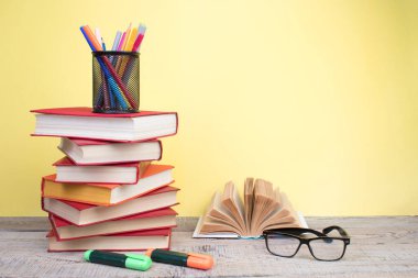 Kapaklı kitaplarla kompozisyon, ahşap güverte masasında sayfalarca yelpaze ve sarı arka plan. Kitaplar istifleniyor. Okula dönelim. Uzayı kopyala Eğitim geçmişi. Okul taksiti.