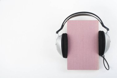 Audiobook beyaz arka plan üzerinde. Kulaklıklar üzerinde pembe ciltli kitap, boş kapak koymak reklam metin için yer kopyalayın. Uzaktan eğitim, e-öğrenme kavramı
