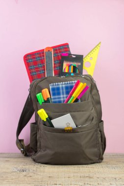 Sırt çantasında farklı renkte kırtasiye malzemeleri var. Pembe arka plan. Okula geri dön.