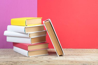 Kitaplar istifleniyor. Ahşap masadaki kitaplar ve kırmızı, mor arka plan. Okula dönelim. Reklam metni için alanı kopyala