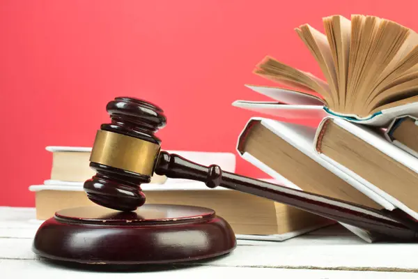 Law concept - Open law book, Judge\'s gavel, scales, Themis statue on table in a courtroom or law enforcement office. Wooden table, red background