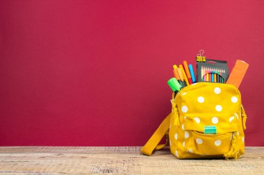 Sırt çantasında farklı renkte kırtasiye malzemeleri var. Burgonya arkaplanı. Okula geri dön.