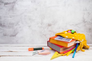 Masada beyaz benekli sarı sırt çantası ve farklı renkli kırtasiye kağıtları var. gri beton arka plan. Okula dönelim. Pankart tasarımı