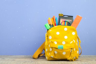 Sırt çantasında farklı renkte kırtasiye malzemeleri var. Mor arka plan. Okula geri dön.