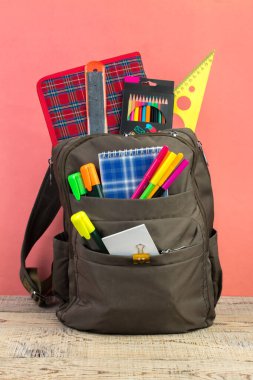 Sırt çantasında farklı renkte kırtasiye malzemeleri var. Pembe arka plan. Okula geri dön.