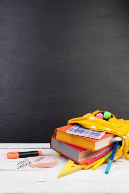Masada beyaz benekli sarı sırt çantası ve farklı renkli kırtasiye kağıtları var. Siyah arka plan. Okula geri dön.
