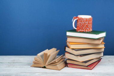 Kitap istifleme. Açık kitap, ahşap masa ve mavi arka plan üzerine ciltli kitaplar. Okula dönelim. Metin için alanı kopyala