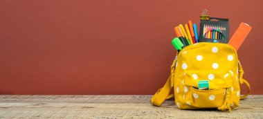 Sırt çantasında farklı renkte kırtasiye malzemeleri var. Kahverengi arka plan. Okula geri dön.
