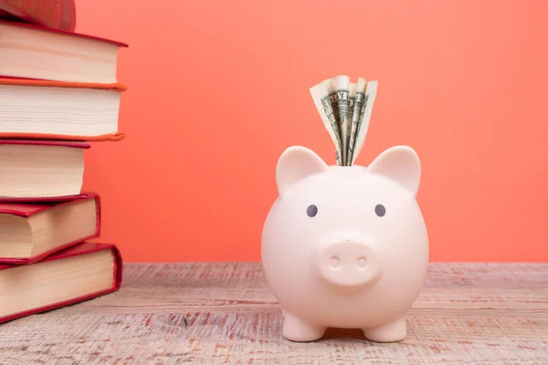 Piggy bank in glasses and books on Orange background. open book. Tuition payment. Brainwork