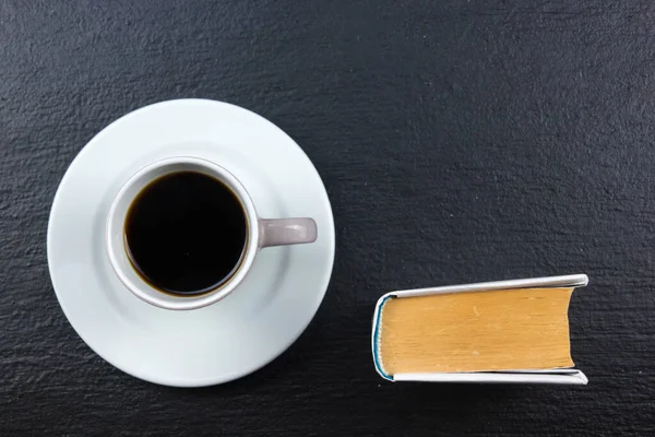 Cup of coffee and book on black wooden background.