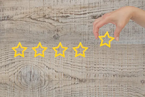 Woman\'s hand put the stars to complete five stars. Customer satisfaction concept. copy space and woode background. giving a five star rating. Service rating, satisfaction concept