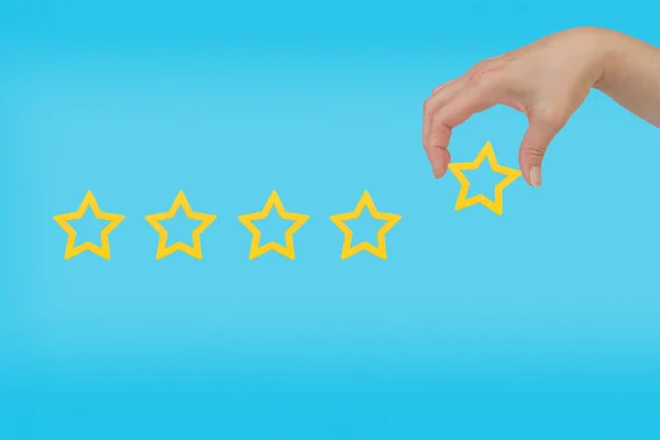 Woman\'s hand put the stars to complete five stars. Customer satisfaction concept. copy space and blue background. giving a five star rating. Service rating, satisfaction concept