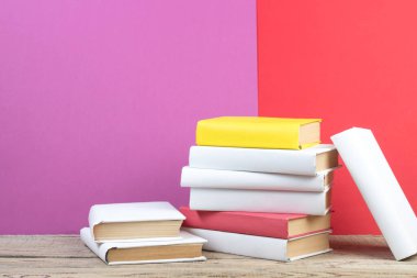 Kitaplar istifleniyor. Ahşap masadaki kitaplar ve kırmızı, mor arka plan. Okula dönelim. Reklam metni için alanı kopyala