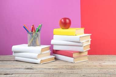 Kitaplar istifleniyor. Ahşap masadaki kitaplar ve kırmızı, mor arka plan. Okula dönelim. Reklam metni için alanı kopyala