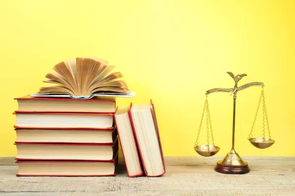 stock image Law concept - Open law book, Judge's gavel, scales, Themis statue on table in a courtroom or law enforcement office. Wooden table, yellow background.