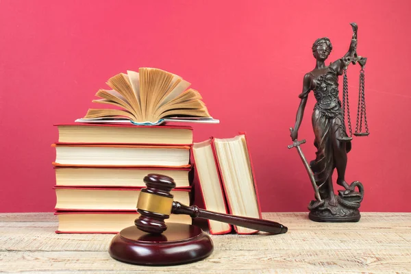 Law concept - Open law book, Judge\'s gavel, scales, Themis statue on table in a courtroom or law enforcement office. Wooden table, red background.