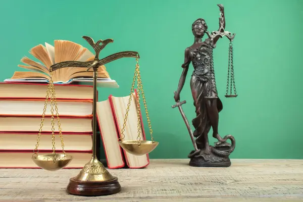 Law concept - Open law book, Judge's gavel, scales, Themis statue on table in a courtroom or law enforcement office. Wooden table, green background.