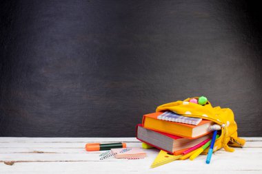 Masada beyaz benekli sarı sırt çantası ve farklı renkli kırtasiye kağıtları var. Siyah arka plan. Okula geri dön.