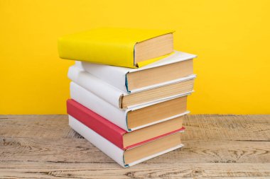 Kitaplar istifleniyor. Tahta masadaki kitaplar ve sarı arka plan. Okula dönelim. Reklam metni için alanı kopyala