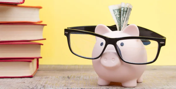 Piggy bank in glasses and books on yellow background. open book. Tuition payment. Brainwork