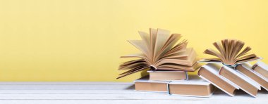 Açık kitaplar, ahşap masada ciltli renkli kitaplar. Sarı arka plan. Okula dönelim. Uzayı metin için kopyala. Eğitim sektörü kavramı