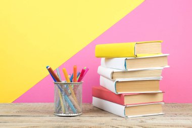 Kitaplar istifleniyor. Tahta masadaki kitaplar ve pembe, sarı arka plan. Okula dönelim. Reklam metni için alanı kopyala