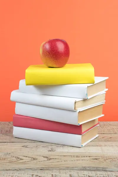 Books stacking. Books on wooden table and orange background. Back to school. Copy space for ad text