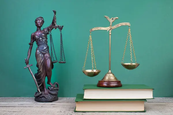 stock image Law concept - Open law book, Judge's gavel, scales, Themis statue on table in a courtroom or law enforcement office. Wooden table, green background.