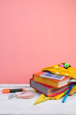 Sırt çantasında farklı renkte kırtasiye malzemeleri var. Pembe arka plan. Okula geri dön.