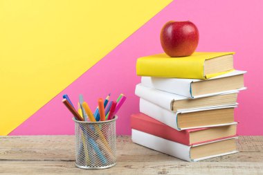 Kitaplar istifleniyor. Tahta masadaki kitaplar ve pembe, sarı arka plan. Okula dönelim. Reklam metni için alanı kopyala