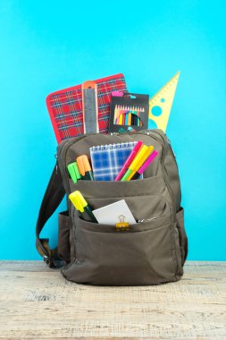 Sırt çantasında farklı renkte kırtasiye malzemeleri var. Mavi arka plan. Okula geri dön.