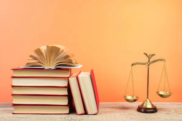 Law concept - Open law book, Judge\'s gavel, scales, Themis statue on table in a courtroom or law enforcement office. Wooden table, orange background.