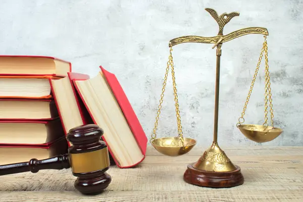 Law concept - Open law book, Judge's gavel, scales, Themis statue on table in a courtroom or law enforcement office. Wooden table, gray concrete background.