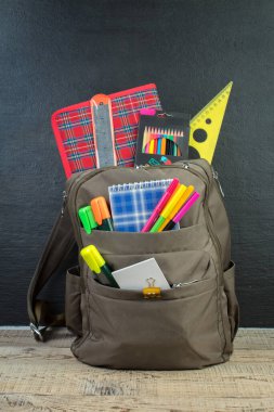 Sırt çantasında farklı renkte kırtasiye malzemeleri var. Siyah arka plan. Okula geri dön.