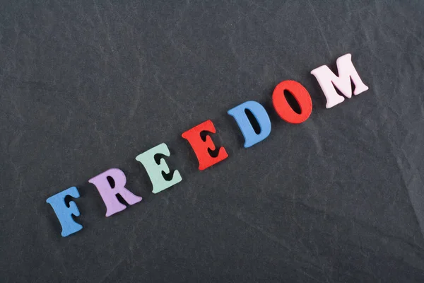 FREEDOM word on black board background composed from colorful abc alphabet block wooden letters, copy space for ad text. Learning english concept