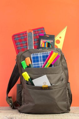 Sırt çantasında farklı renkte kırtasiye malzemeleri var. Turuncu arka plan. Okula geri dön.