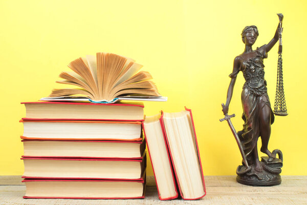 Law concept - Open law book, Judge's gavel, scales, Themis statue on table in a courtroom or law enforcement office. Wooden table, yellow background.
