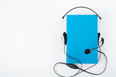 Beyaz arka planda Audiobook. Kulaklıklar mavi kaplı defter, boş kapak, reklam metni için kopyalama alanı. Uzaklık eğitimi, e-öğrenme kavramı