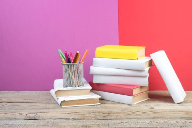 Kitaplar istifleniyor. Ahşap masadaki kitaplar ve kırmızı, mor arka plan. Okula dönelim. Reklam metni için alanı kopyala