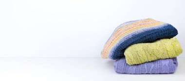 Yünlü yün kazaklar. Bir demet örülmüş kış, arka planda sonbahar kıyafetleri, süveterler, örgü giysiler, yazı için yer. Pankart