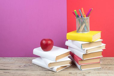 Kitaplar istifleniyor. Ahşap masadaki kitaplar ve kırmızı, mor arka plan. Okula dönelim. Reklam metni için alanı kopyala
