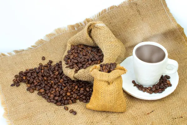 Opened burlap bags, a cup of coffee, scattered whole coffee beans on a white background