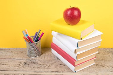 Kitaplar istifleniyor. Tahta masadaki kitaplar ve sarı arka plan. Okula dönelim. Reklam metni için alanı kopyala