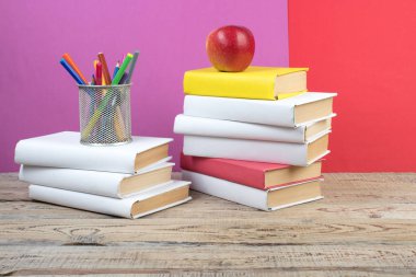 Kitaplar istifleniyor. Ahşap masadaki kitaplar ve kırmızı, mor arka plan. Okula dönelim. Reklam metni için alanı kopyala