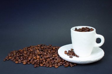 Bir yığın kahve çekirdeği, koyu arkaplanda beyaz bir fincan kahve. Ön görünüm