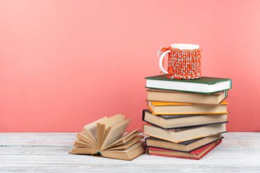 Kitap istifleme. Açık bir kitap, ahşap masa ve pembe arka plan üzerine ciltli kitaplar. Okula dönelim. Metin için alanı kopyala